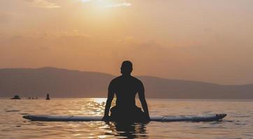 Sporty young man on SUP paddle board going to the sea at sunset. photo