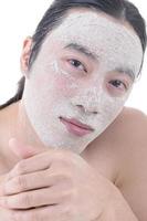 Beauty procedures skin care concept. Young man applying facial gray mud clay mask on his face photo