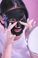 Young beautiful woman posing with black cosmetic mask on her face photo