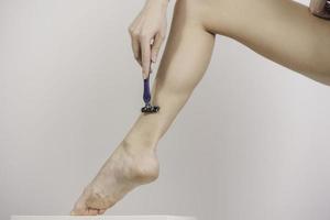 young woman shaving her legs with razor photo