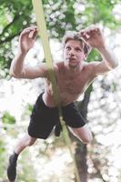 Young man balancing and jumping on slackline. Man walking, jumping and balancing on rope in park. photo