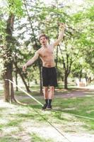 Young man balancing and jumping on slackline. Man walking, jumping and balancing on rope in park. photo