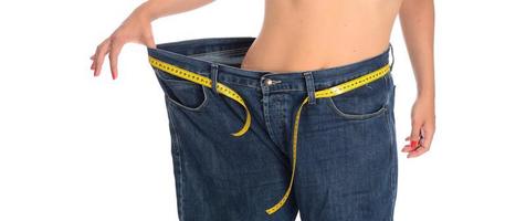 mid section of a woman with belly fat holding her blue jeans. Girl with big jeans isolated on white background. Woman shows her weight loss. Healthy lifestyle concept photo
