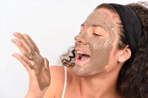 Beauty procedures skin care concept. Young woman applying facial gray mud clay mask to her face photo