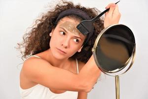 Beauty procedures skin care concept. Young woman applying facial gray mud clay mask to her face photo