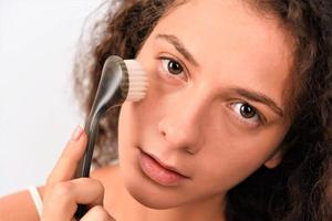 Beautiful young woman is washing her face with face brush photo