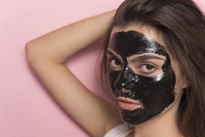 Young beautiful woman posing with black cosmetic mask on her face photo