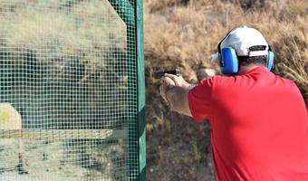 vista trasera de un hombre disparando su arma en un rancho de práctica. foto