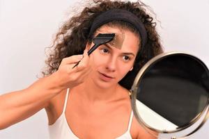 Beauty procedures skin care concept. Young woman applying facial gray mud clay mask to her face photo