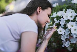 mujer joven en un vivero sosteniendo una planta de flores en sus manos mientras se arrodilla en el camino entre las plantas. foto