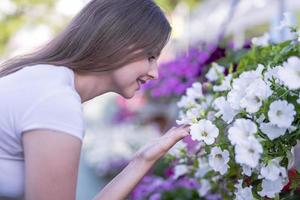 mujer joven en un vivero sosteniendo una planta de flores en sus manos mientras se arrodilla en el camino entre las plantas. foto