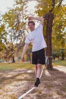 Young man balancing and jumping on slackline. Man walking, jumping and balancing on rope in park. photo