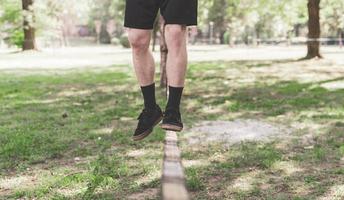 Young man balancing and jumping on slackline. Man walking, jumping and balancing on rope in park. photo