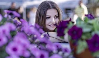 mujer joven en un vivero sosteniendo una planta de flores en sus manos mientras se arrodilla en el camino entre las plantas. foto