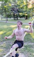 Young man balancing and jumping on slackline. Man walking, jumping and balancing on rope in park. photo