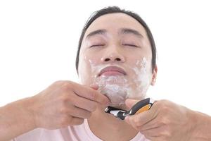 Close up portrait of a Asian man with shaving foam on his face, shaving his beard with razor. isolated over white background