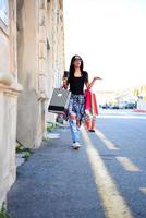 hermosa mujer caminando por la calle con bolsas de compras. modelo femenino de moda en la ciudad con bolsas de compras. foto