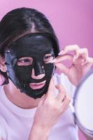 Young beautiful woman posing with black cosmetic mask on her face photo