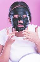 Young beautiful woman posing with black cosmetic mask on her face photo