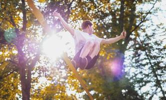 Young man balancing and jumping on slackline. Man walking, jumping and balancing on rope in park. photo