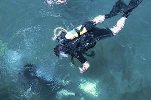 Top view of scuba diver swimming under water and examines the seabed. Scuba diver bubbles coming from bottom to surface. photo