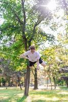 Young man balancing and jumping on slackline. Man walking, jumping and balancing on rope in park. photo