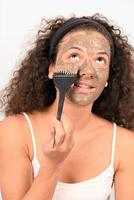 Beauty procedures skin care concept. Young woman applying facial gray mud clay mask to her face photo