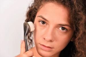 Beautiful young woman is washing her face with face brush photo