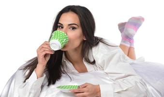 hermosa mujer morena acostada en cuentas sosteniendo una taza de café, una taza de té foto