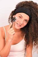 Beautiful young woman is washing her face with face brush photo