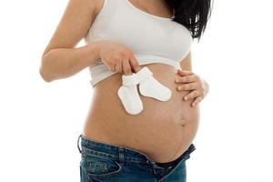 close up of pregnant brunette woman with little white socks in her hands isolated in studio photo