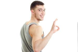 handsome young sporty guy stands sideways looks forward smiles and hand gesture Okey photo