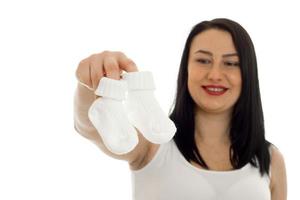 hermosa mujer embarazada posando con pequeños calcetines en las manos aislado sobre fondo blanco. foto