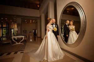 beautiful young just merried couple posing in front of a large mirror photo