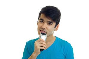 young attractive guy in the blue shirt shaves his beard shaving machine photo