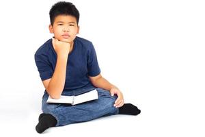 Young asian boy sitting cross-legged, with resting his chin on his hand and a book on his thigh. Education and learning concept. photo