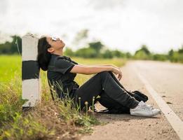 Woman sit with backpack hitchhiking along a road in countryside photo