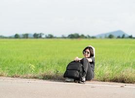 Woman sit with backpack hitchhiking along a road photo