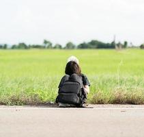 Woman sit with backpack hitchhiking along a road photo