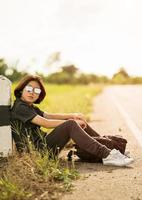 Woman sit with backpack hitchhiking along a road in countryside photo