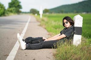 Woman sit with backpack hitchhiking along a road in countryside photo