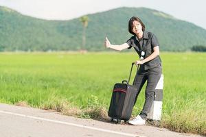 mujer de pelo corto con equipaje haciendo autostop y pulgares arriba foto