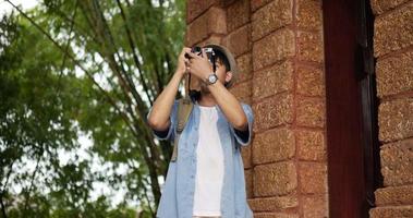 Happy asian traveler man with hat takes a photo and visits ancient temple. Smiling young male walking and holding camera. Holiday, travel and hobby concept. video