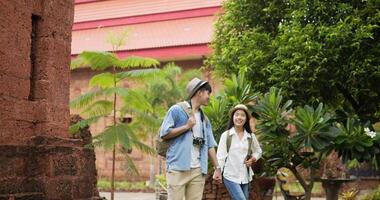 Happy asian traveler couple with hat hand together while visiting at ancient temple. Smiling young man and woman walking and looking ancient temple. Holiday, travel and hobby concept. video