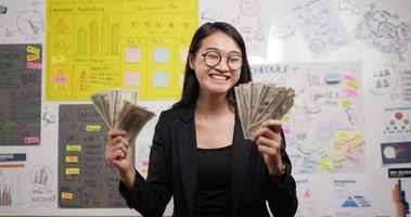 Portrait of successful asian businesswoman glasses throwing banknotes in office. Happy rich millionaire throws cash. Confident female manager celebrating victory with cash. video