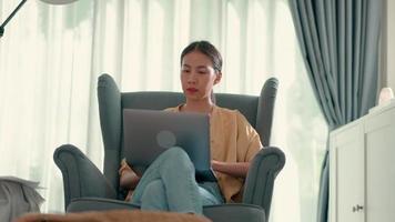 mujer bonita joven sentada en el sofá y se alegra cuando tiene una buena idea y escribe en una computadora portátil, nueva normalidad y concepto de trabajo desde casa video