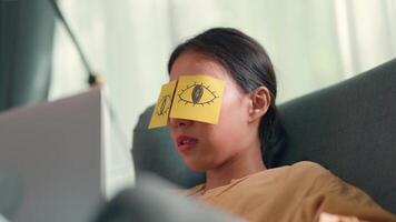 mujer graciosa y de mano coloca los ojos abiertos en el papel y colóquelos en los ojos sintiéndose exhausta y quedándose dormida durante el trabajo desde casa video