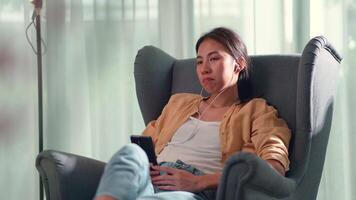 Young woman sitting on sofa in living room and use earphone for listening and talking with someone on smartphone at home video