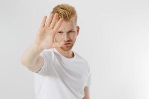 detener el signo de las manos. joven en camiseta blanca de plantilla en blanco que muestra gesto de parada. chico pelirrojo y barba roja aislado. concepto de protección contra riesgos. copia espacio y maqueta en camiseta. enfoque selectivo foto