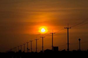 Atmósfera en el poste de alto voltaje de la tarde al lado de la carretera y el cielo anaranjado. El gran sol que se estaba poniendo era hermoso cuando estaba de camino a casa, era una hermosa atmósfera romántica. foto